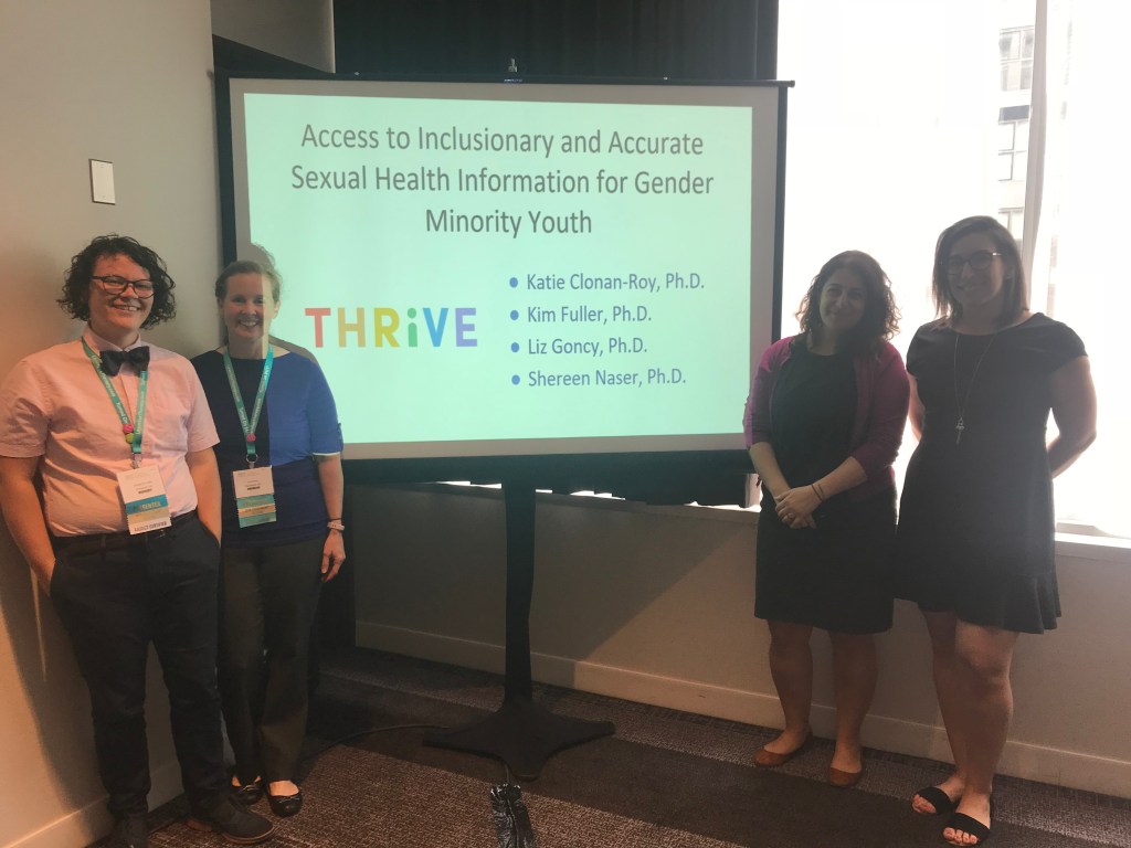 Dr. Kim Fuller, Dr. Liz Goncy, Dr. Shereen Naser, and Dr. Katie Clonan-Roy stand by their presentation slide projected on a conference event screen. The session is on Access to Inclusionary and Accurate Sexual Health Information for Gender Minority Youth, from their THRiVE Research Collaborative